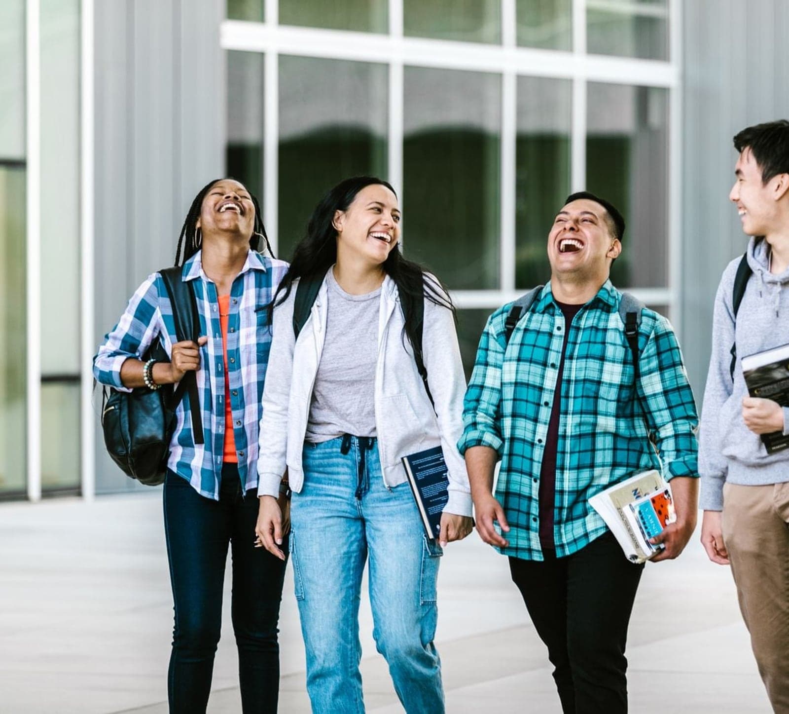 Three students walking together outside a building, carrying books and bags, laughing.