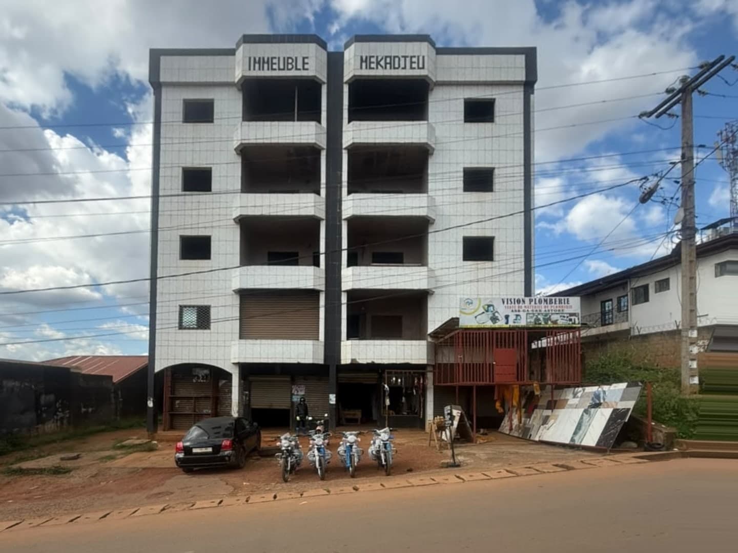 The five-storey building BOLO IT is renovating, lettered Immeuble Hekadjeu across the parapet, with shops and parked motorcycles at street level.