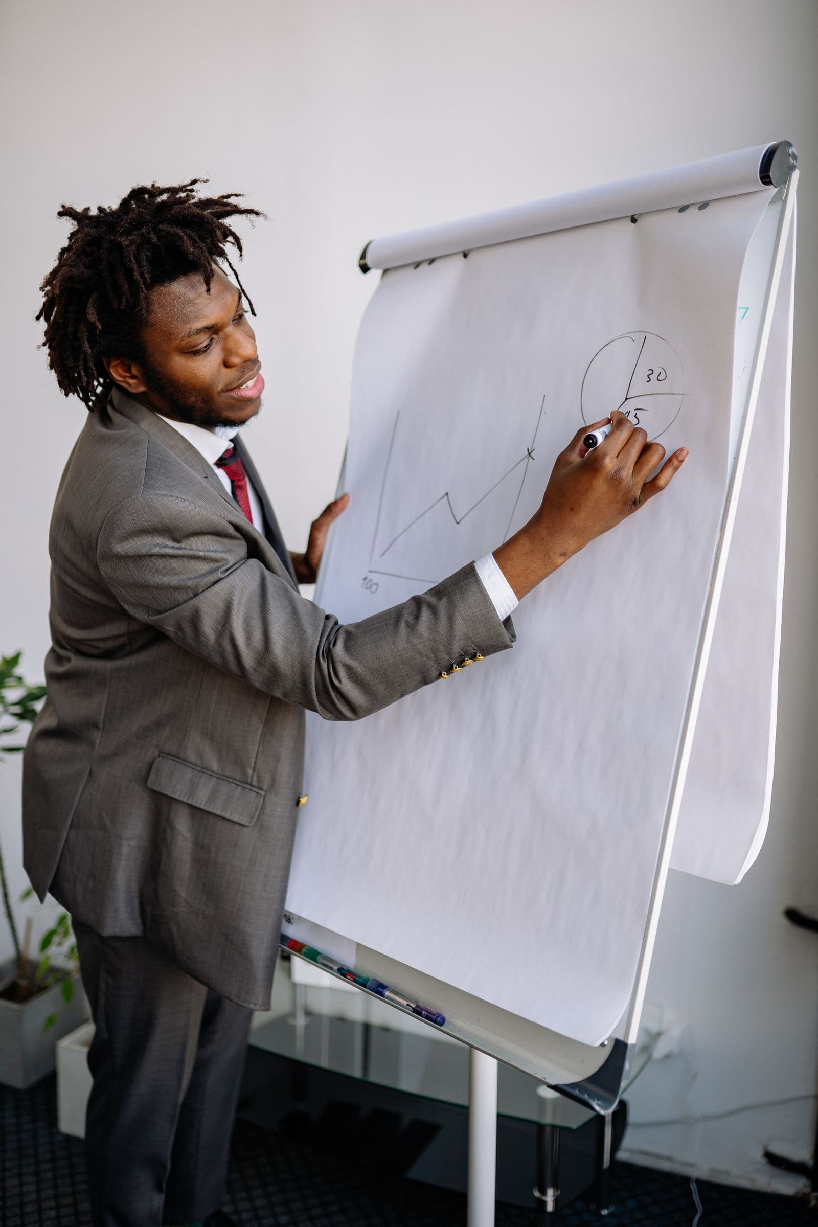 A professional in a suit drawing a chart on a flip chart in a bright office.