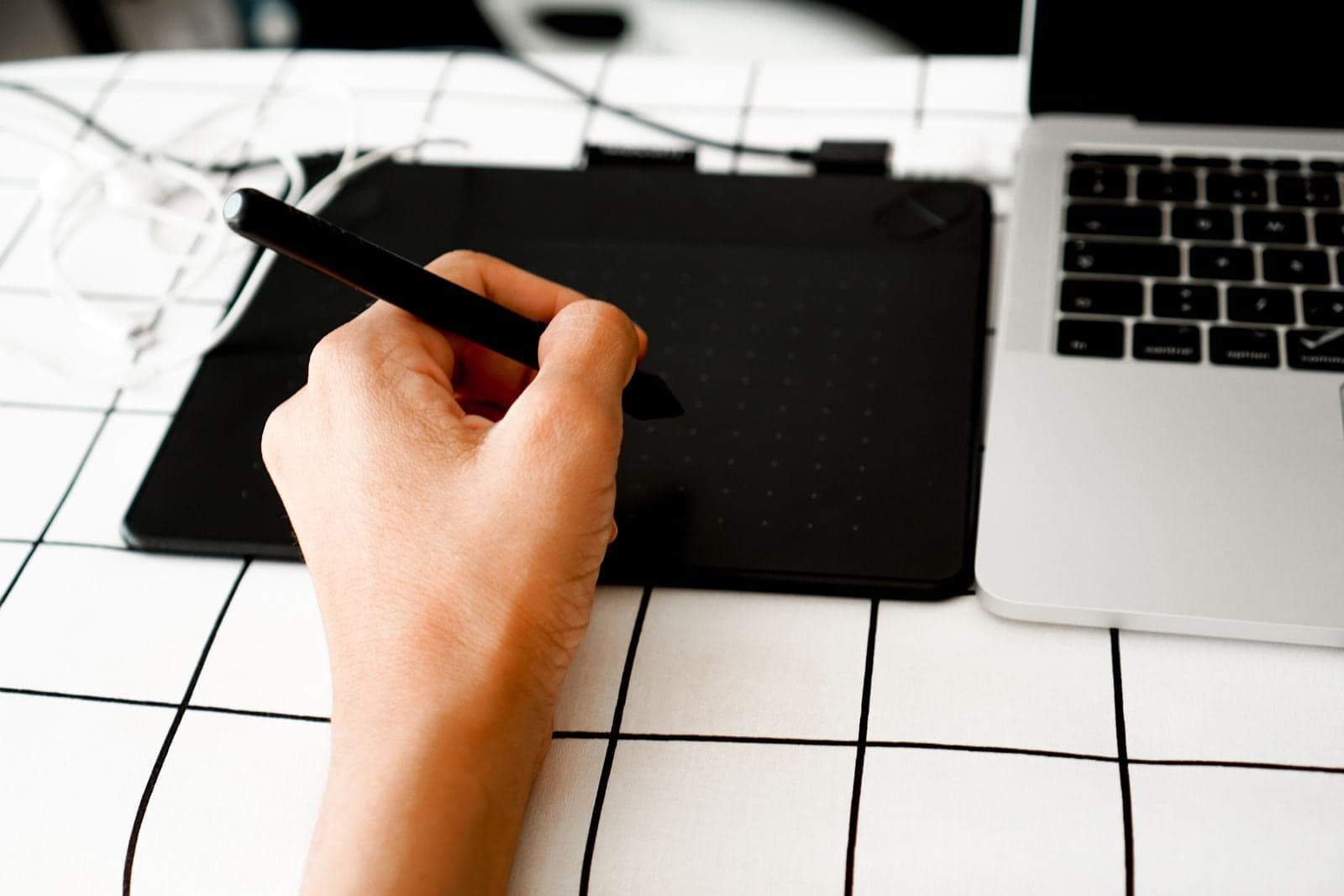 A hand holding a stylus over a graphics tablet beside a laptop.