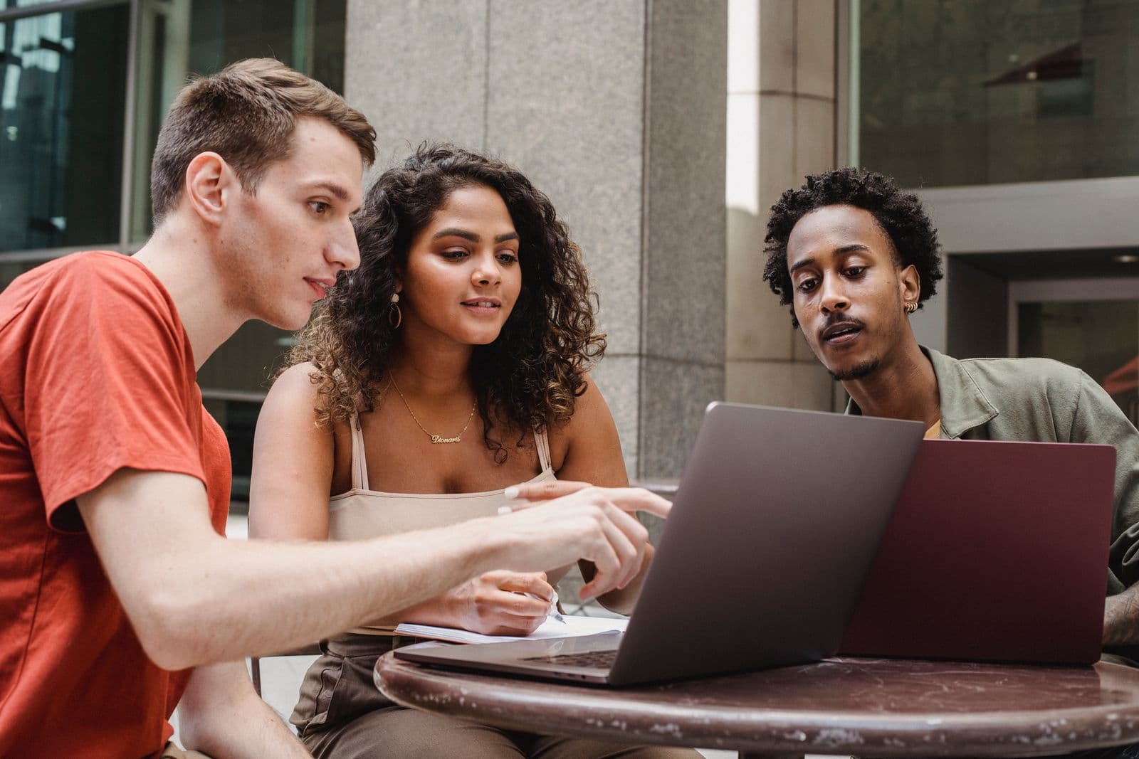 Three people working together at a table, looking at a laptop screen between them.