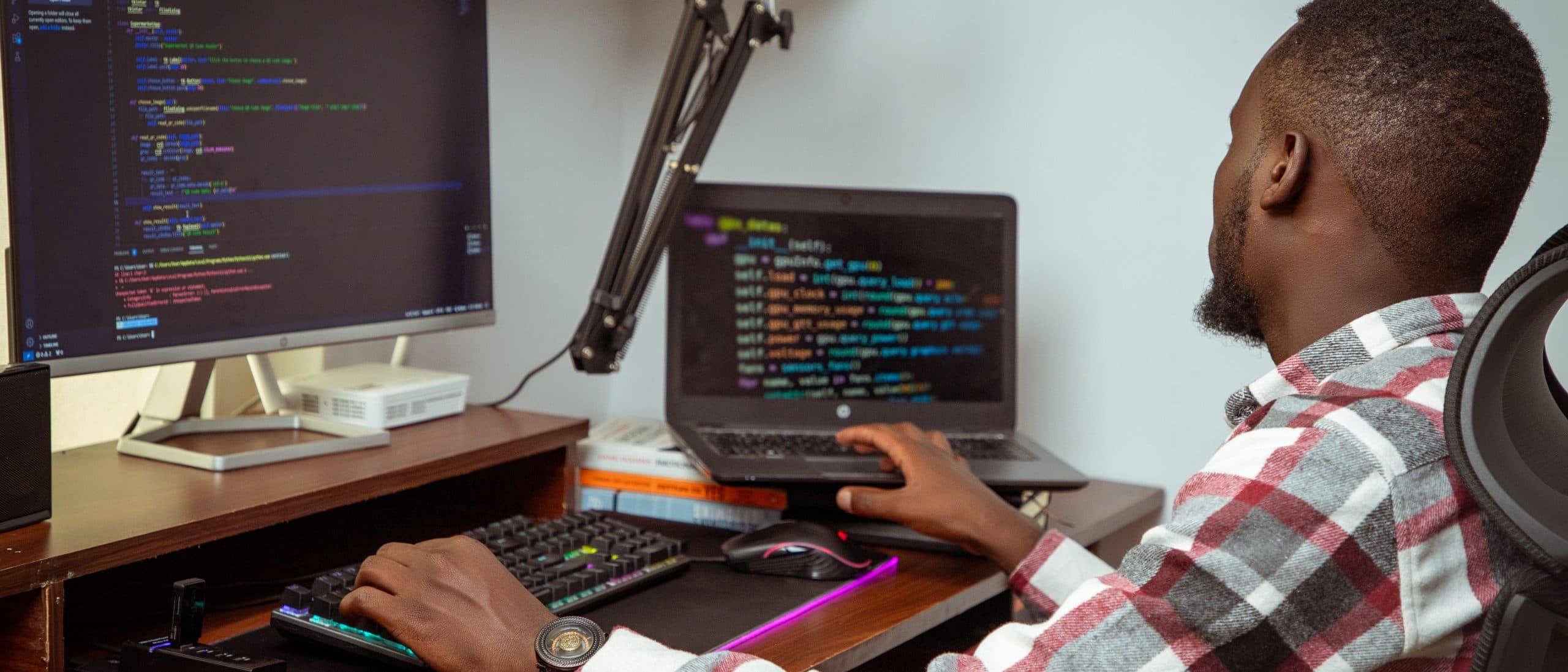 An engineer in Nairobi writing Python across a desktop monitor and a laptop.