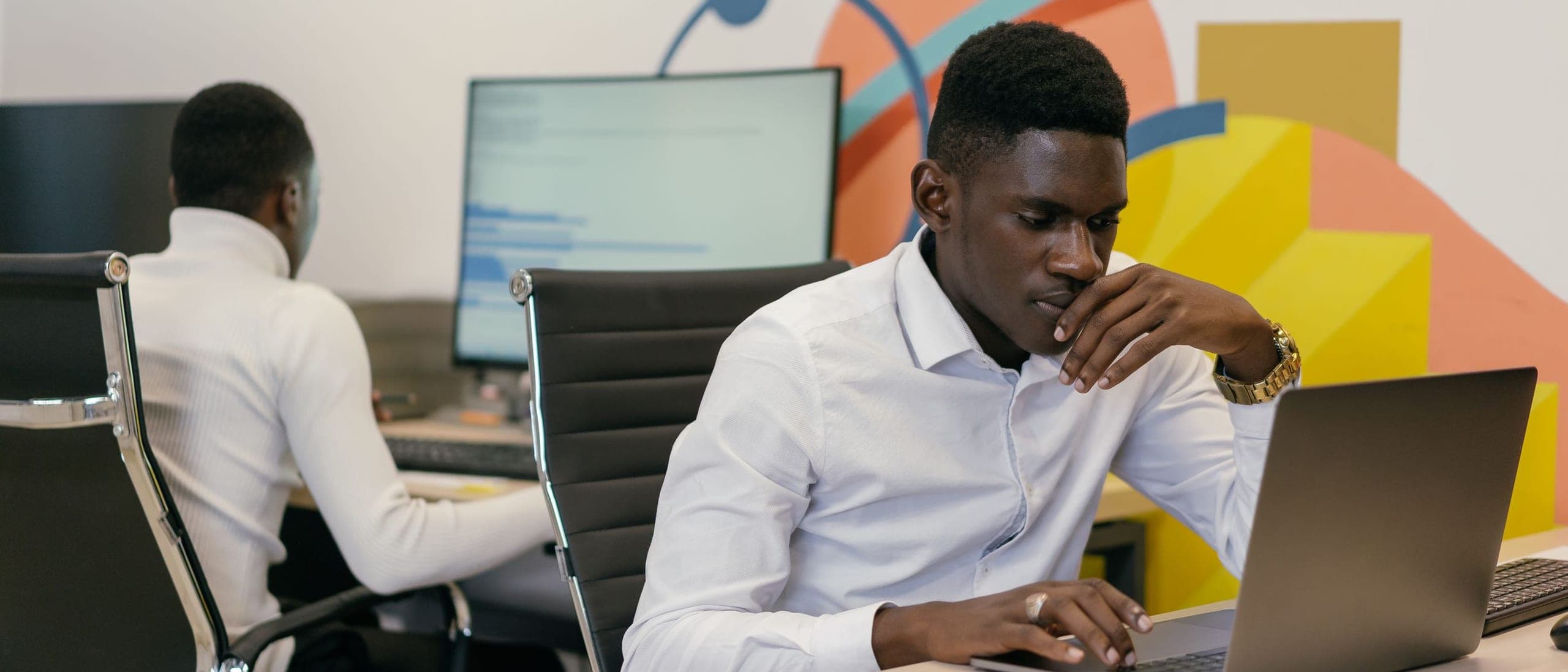 Two engineers at work on laptops in a modern open-plan technology office.